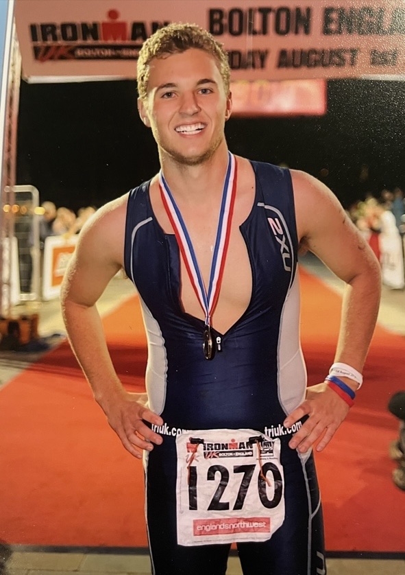 Brian at 18, smiling at the finish line of the Bolton Ironman in England, medal on